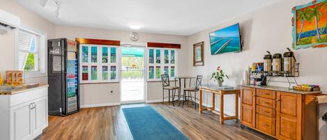 Una cocina con armarios de madera, un refrigerador, una zona de comedor con sillas y vistas a través de las ventanas.