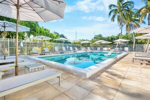 Una piscina al aire libre, sombrillas, sillones reclinables de piscina