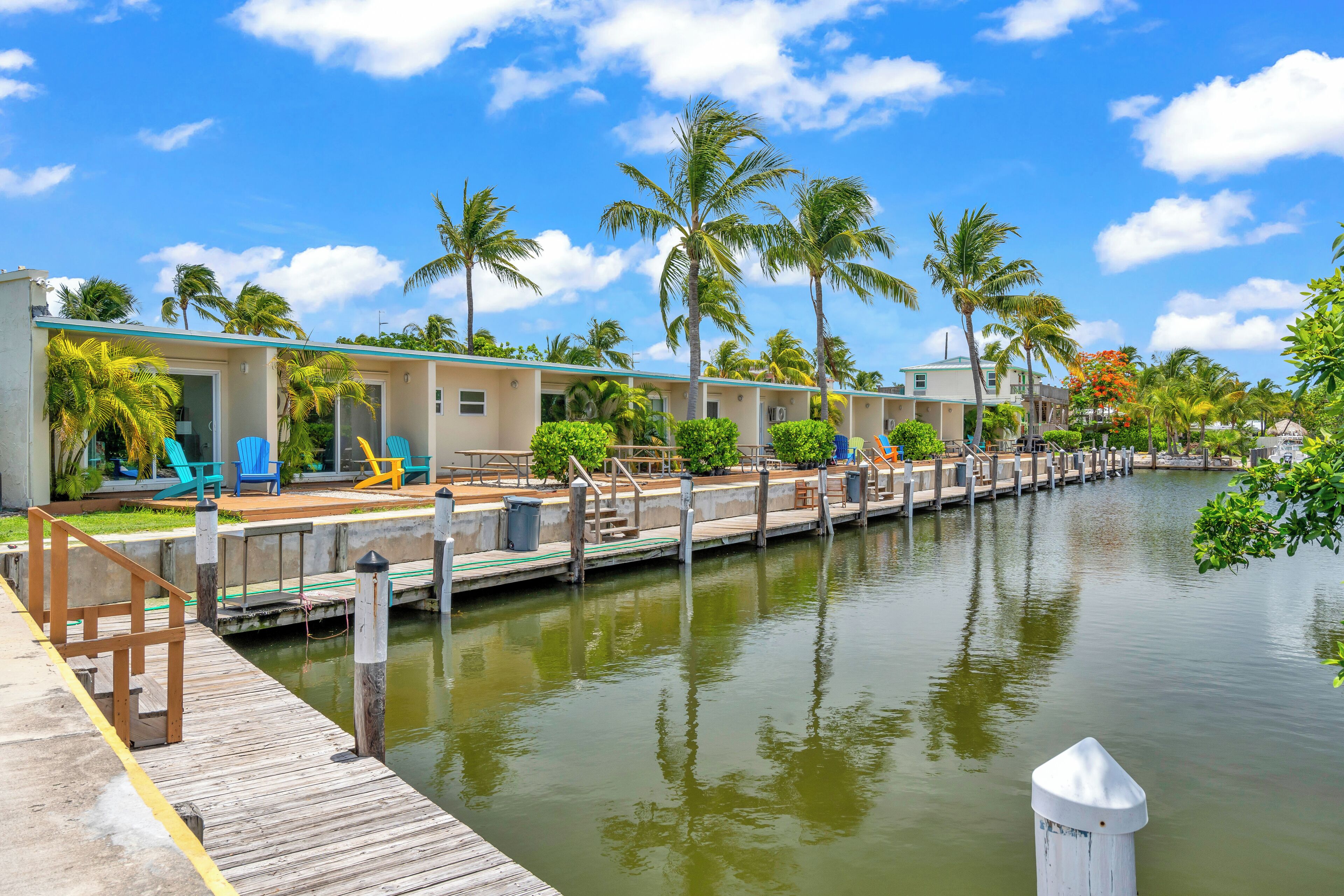 A waterfront hotel with a dock, palm trees, and a clear sky.