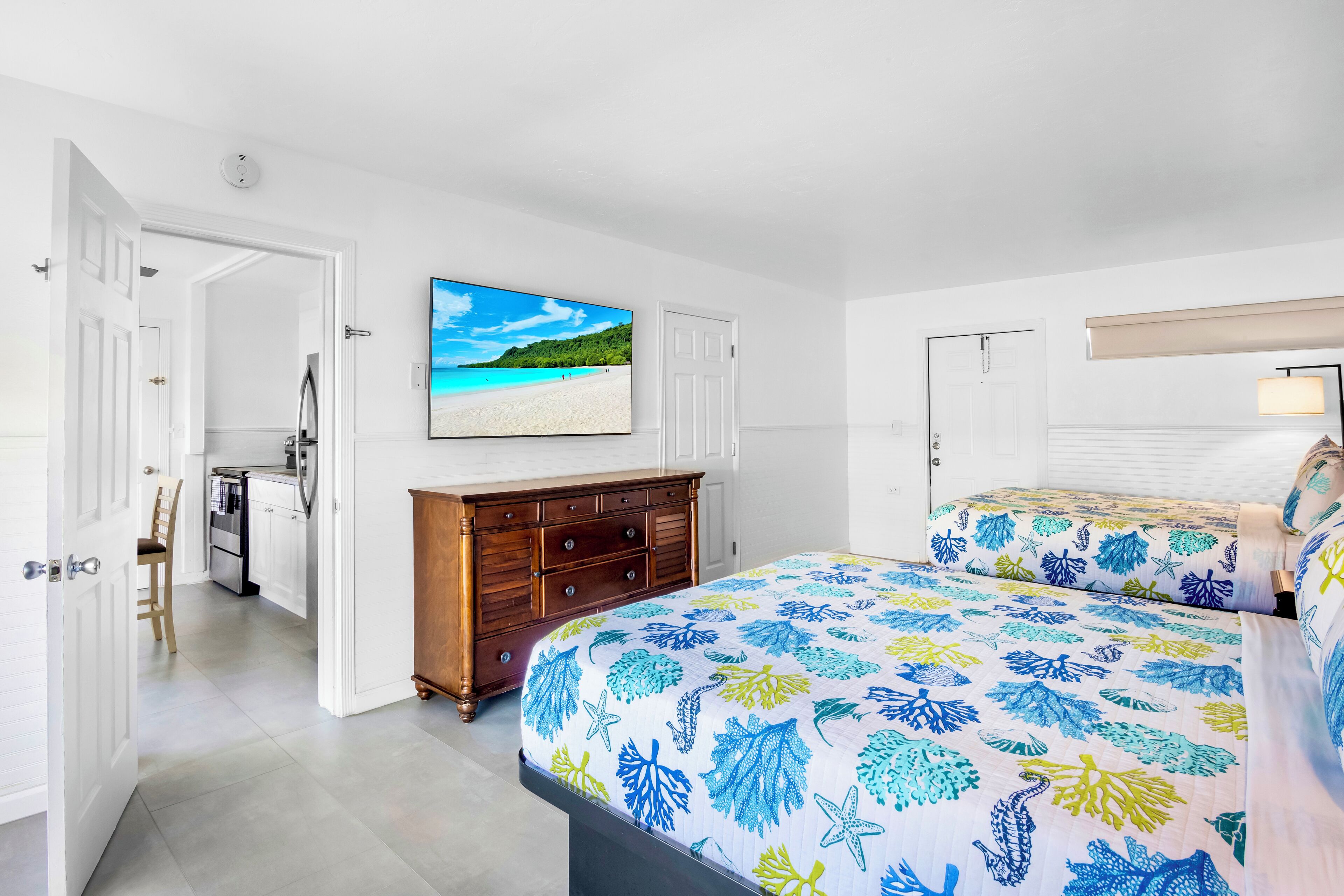 Een slaapkamer met een bed, een dressoir en een schilderij van een strandgezicht.