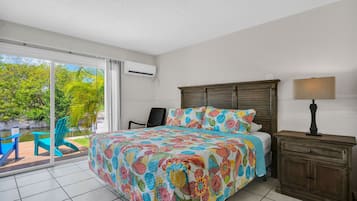 Un dormitorio con una cama grande, una mesita de noche, una silla y vistas a una piscina y vegetación al exterior.