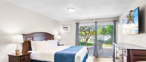 Habitación de hotel con cama, mesita de noche, cómoda, televisor y vistas al exterior.