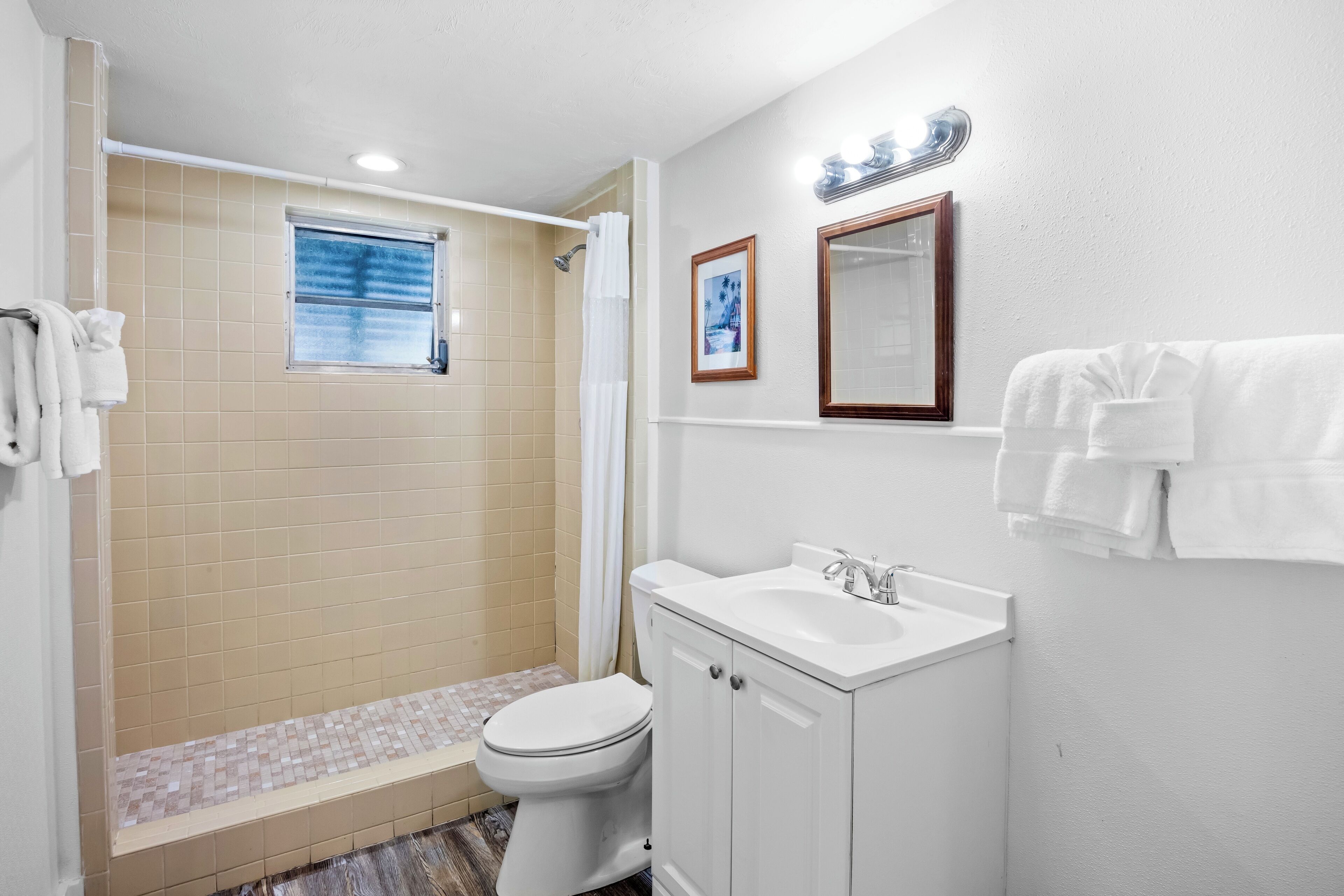 A bathroom with a toilet, sink, and shower. There are towels hanging on the wall and a window above the shower.