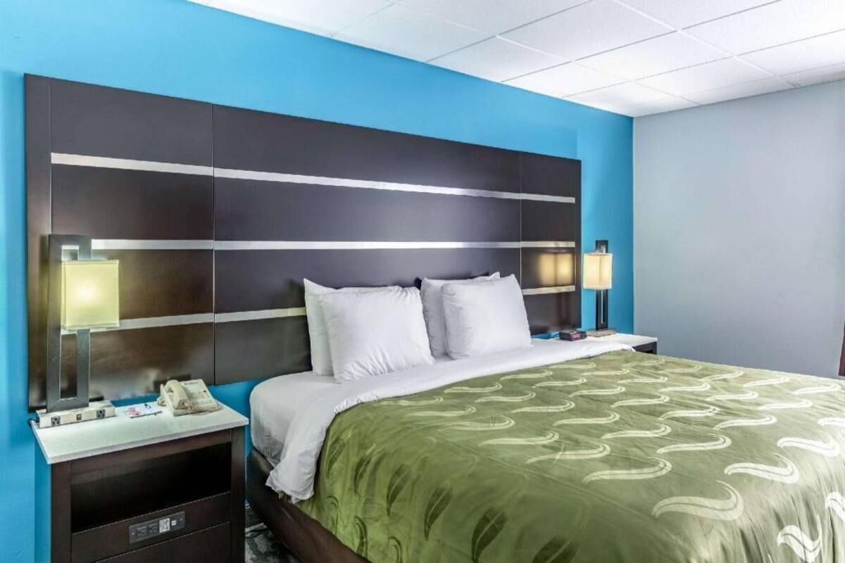 A hotel room with a large bed, two bedside tables, a nightstand, a telephone, and a lamp.