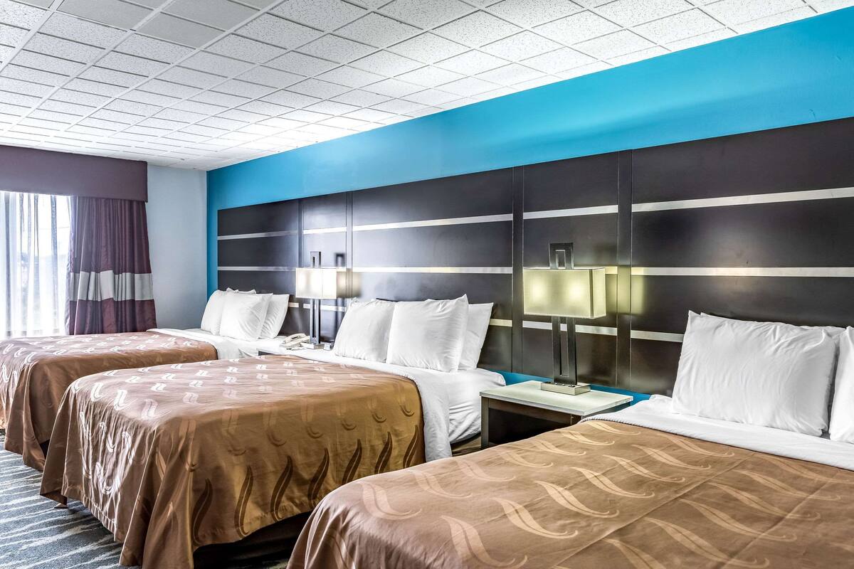 A hotel room with three beds, a large headboard, and a window with curtains.