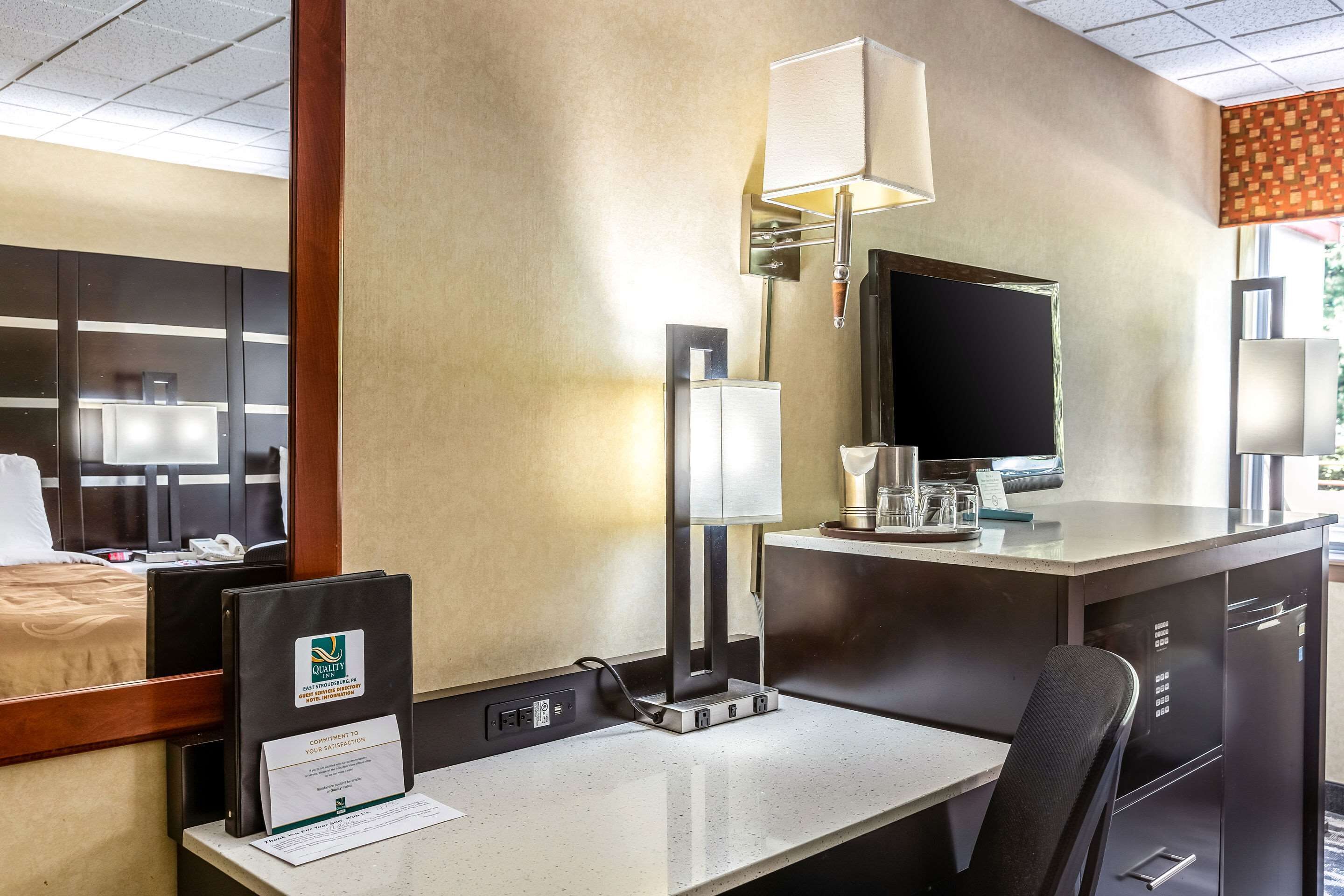 A hotel room with a bed, desk, chair, lamp, and a television.
