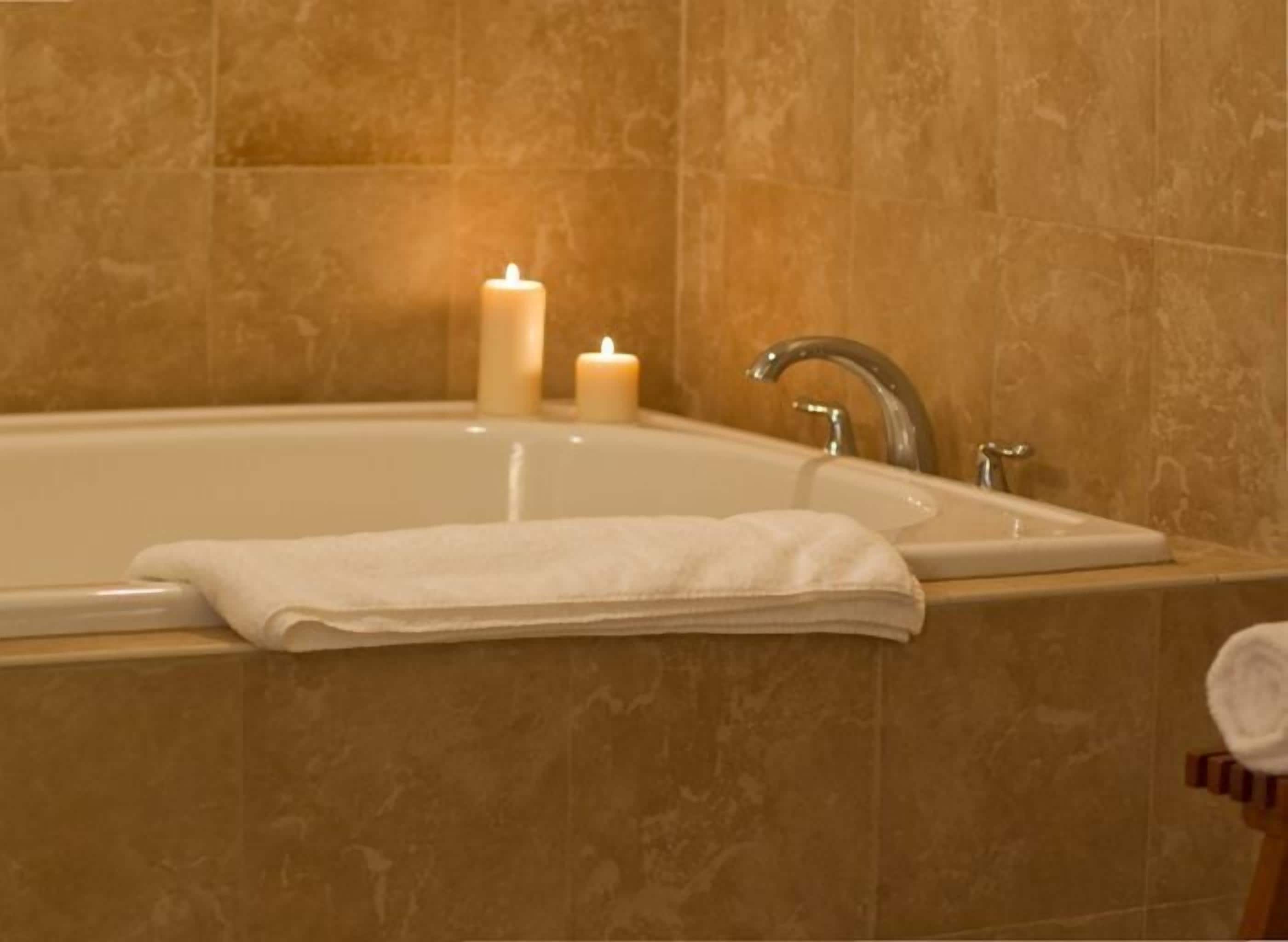 Un baño con una bañera, dos velas encendidas y una toalla sobre el borde.