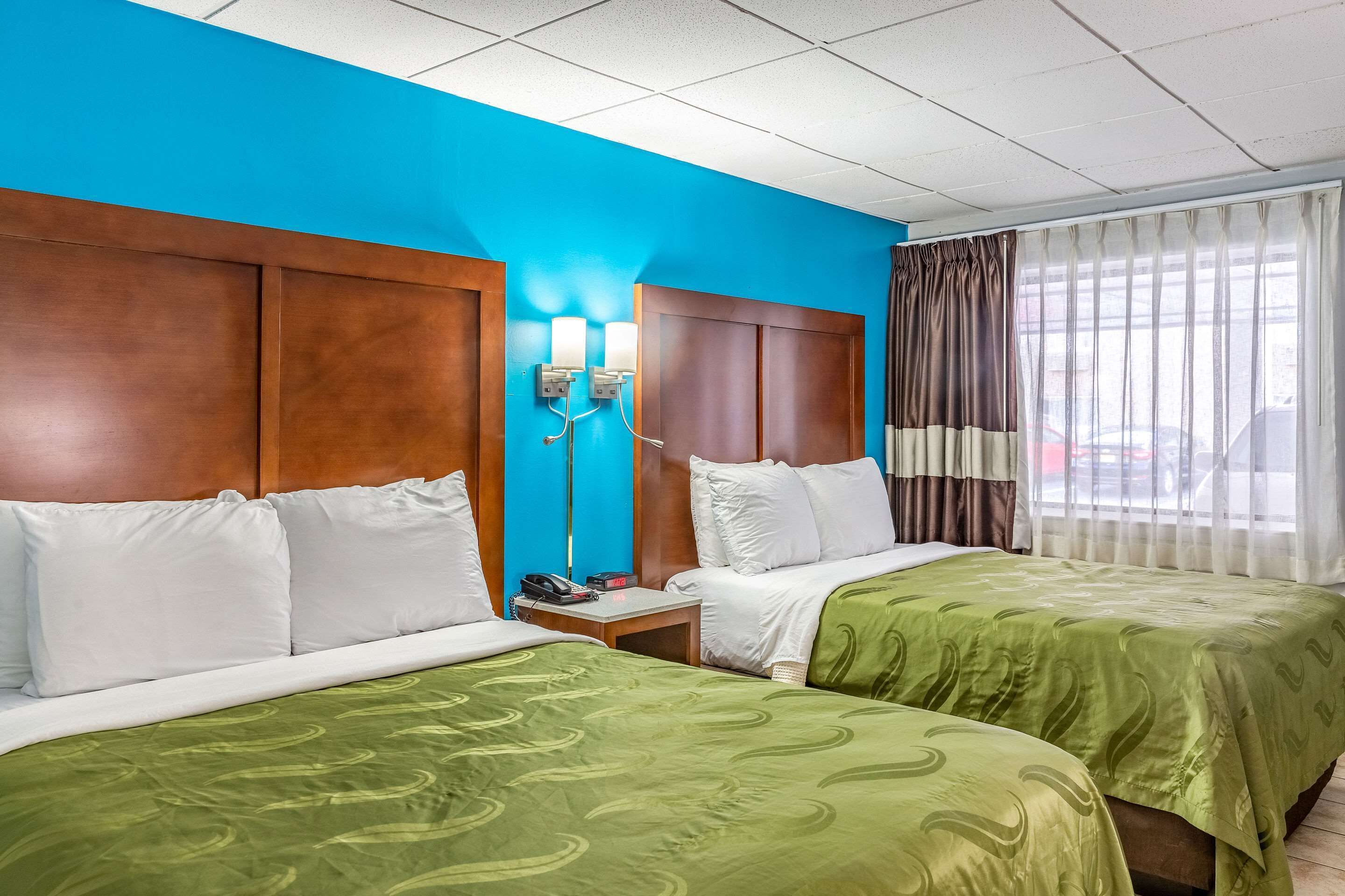 A hotel room with two beds, a nightstand, a telephone, and a window with curtains.