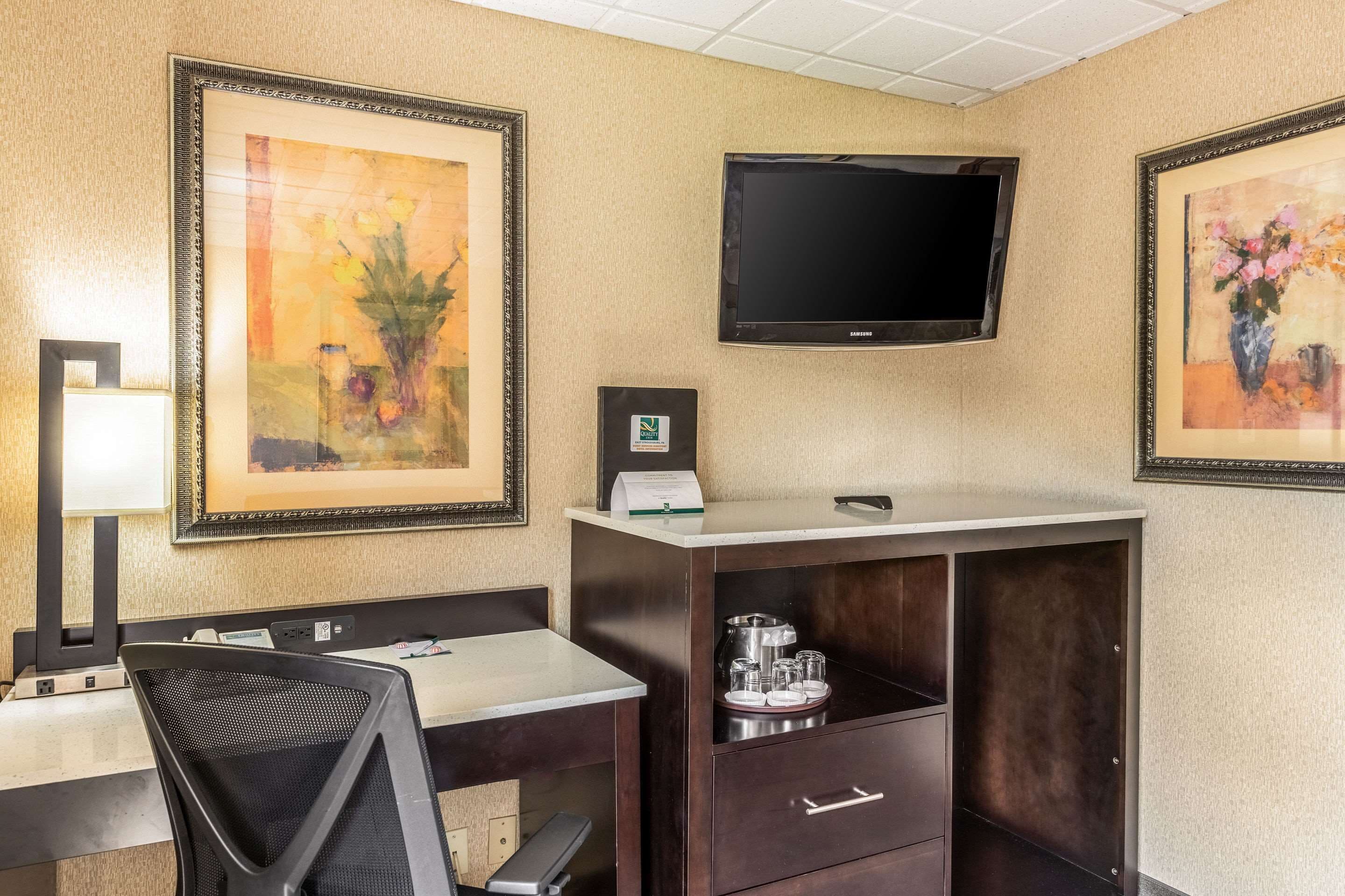 Een hotelkamer met een bureau, stoel, televisie, kunstwerk en een minibar.