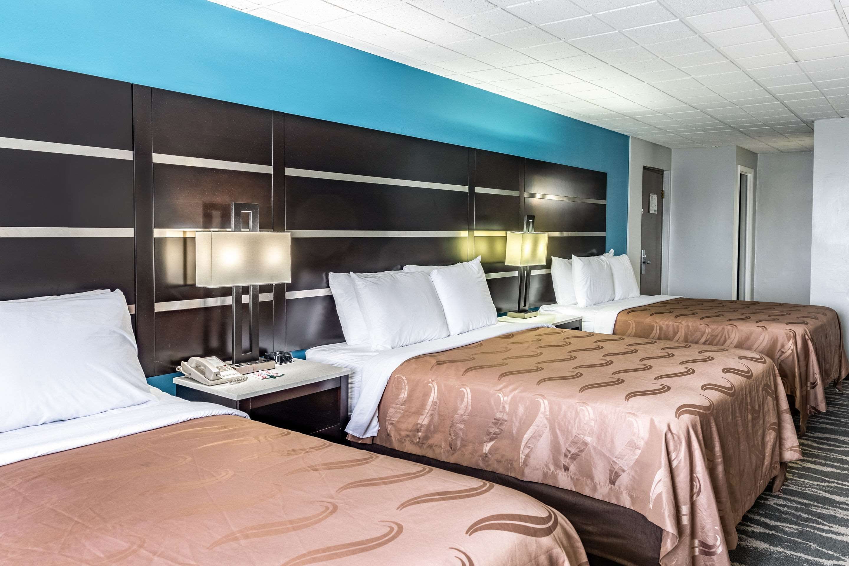 Habitación de hotel con dos camas, un cabecero grande, lámparas de noche y un teléfono en la mesita de noche.