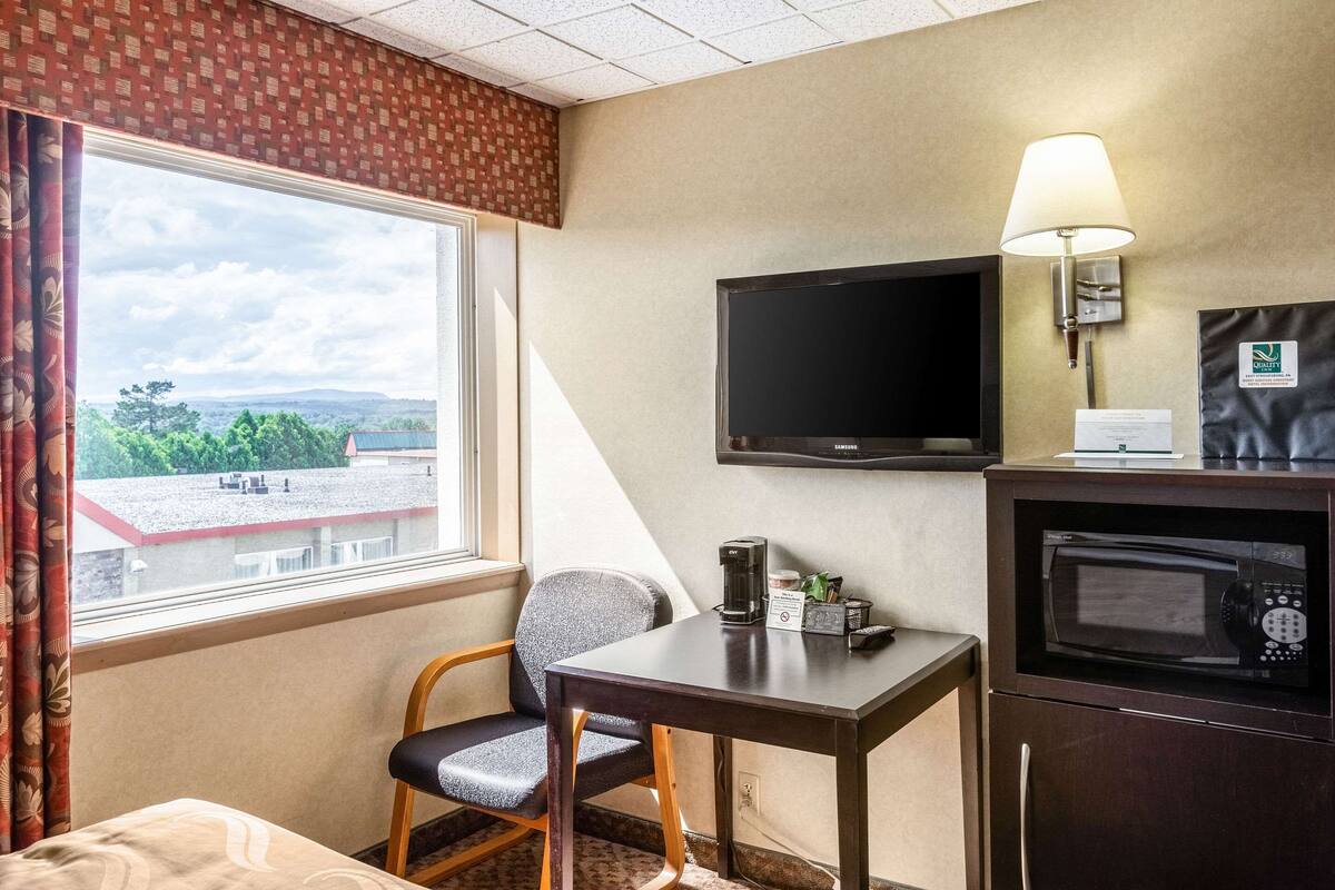 A hotel room with a bed, a desk with a chair, a television, a microwave, and a window with curtains.