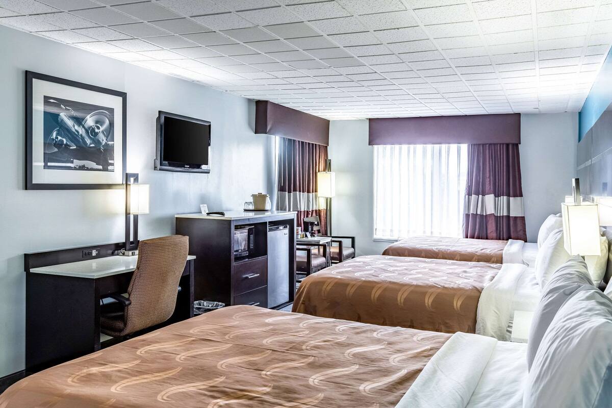 A hotel room with two beds, a desk, a chair, a television, and a window with curtains.