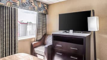 A hotel room with a bed, a desk with a flat-screen TV, a chair, and a dresser.