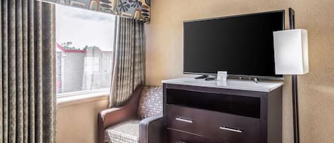 Une chambre d’hôtel comprenant un lit, un bureau avec un téléviseur à écran plat, une chaise et une commode.