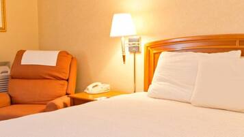 A hotel room with a bed, a nightstand with a lamp, a telephone, and an orange chair.