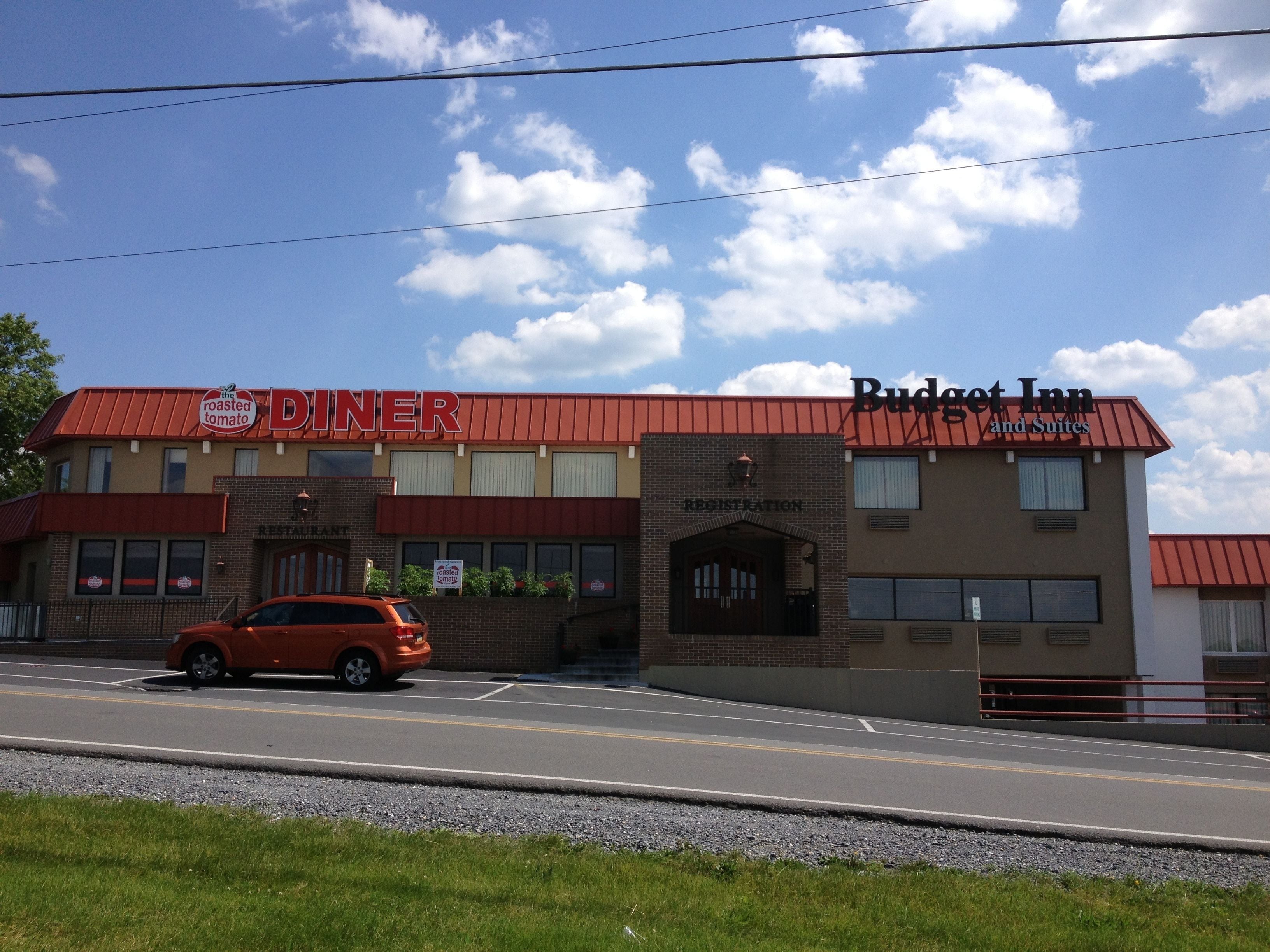 Una tavola calda con tetto rosso e un'insegna che riporta 'The Roasted Tomato Diner'. Accanto, un edificio con l'insegna 'Budget Inn and Suites'.