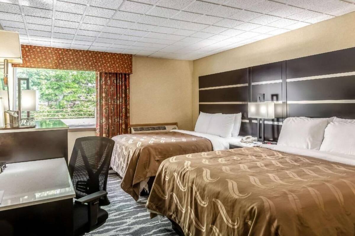 A hotel room with two beds, a desk, a chair, and a window with curtains.