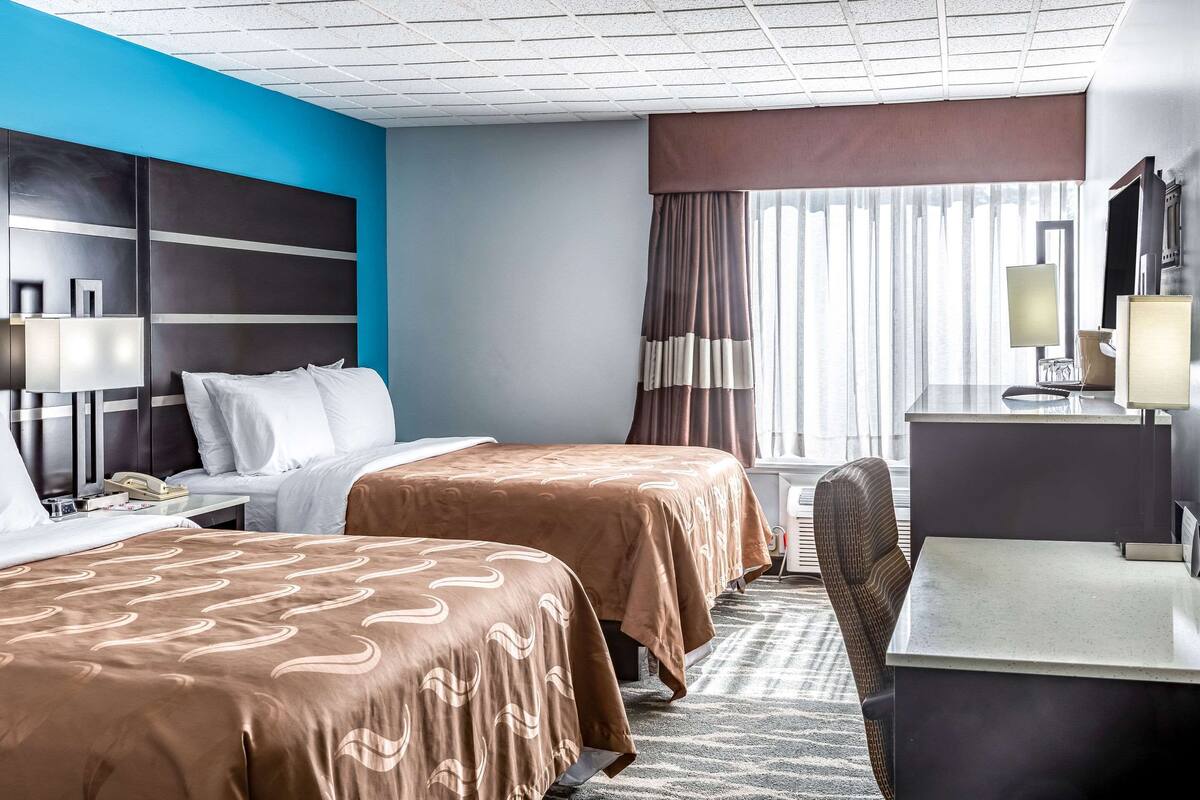 A hotel room with two beds, a desk, a chair, a TV, and a window with curtains.