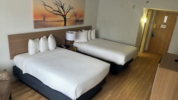 Habitación de hotel con dos camas, una mesita de noche, una lámpara, un cuadro de un árbol y una puerta de madera.