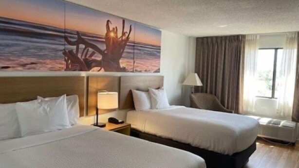 A hotel room with two beds, a large painting of a sunset, a chair, and a window with curtains. - Days Inn by Wyndham Sherman (Sherman)