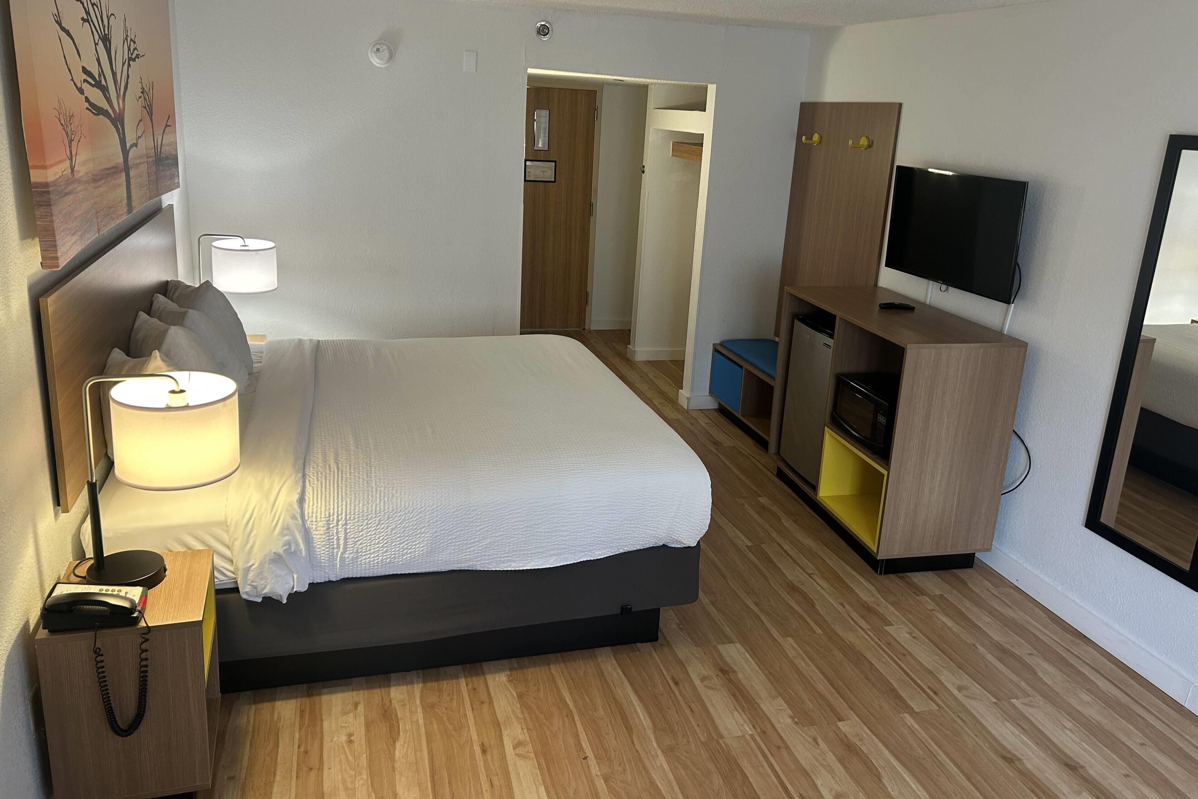 A hotel room with a bed, bedside lamp, TV, wooden cabinet, and a door leading to another room.