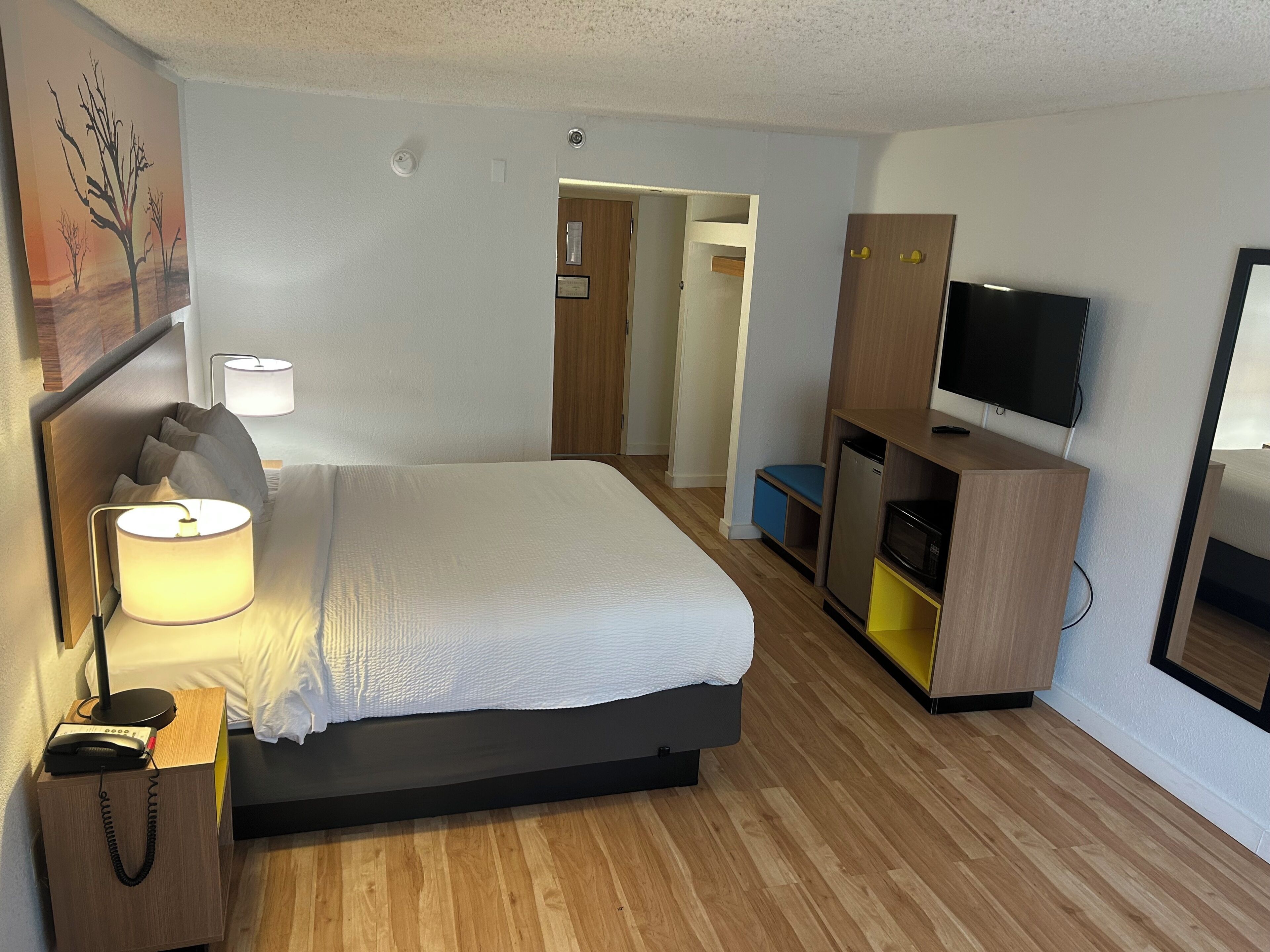 Una camera d'albergo con un letto, lampade sui comodini, una scrivania con un telefono, una televisione e un armadio.