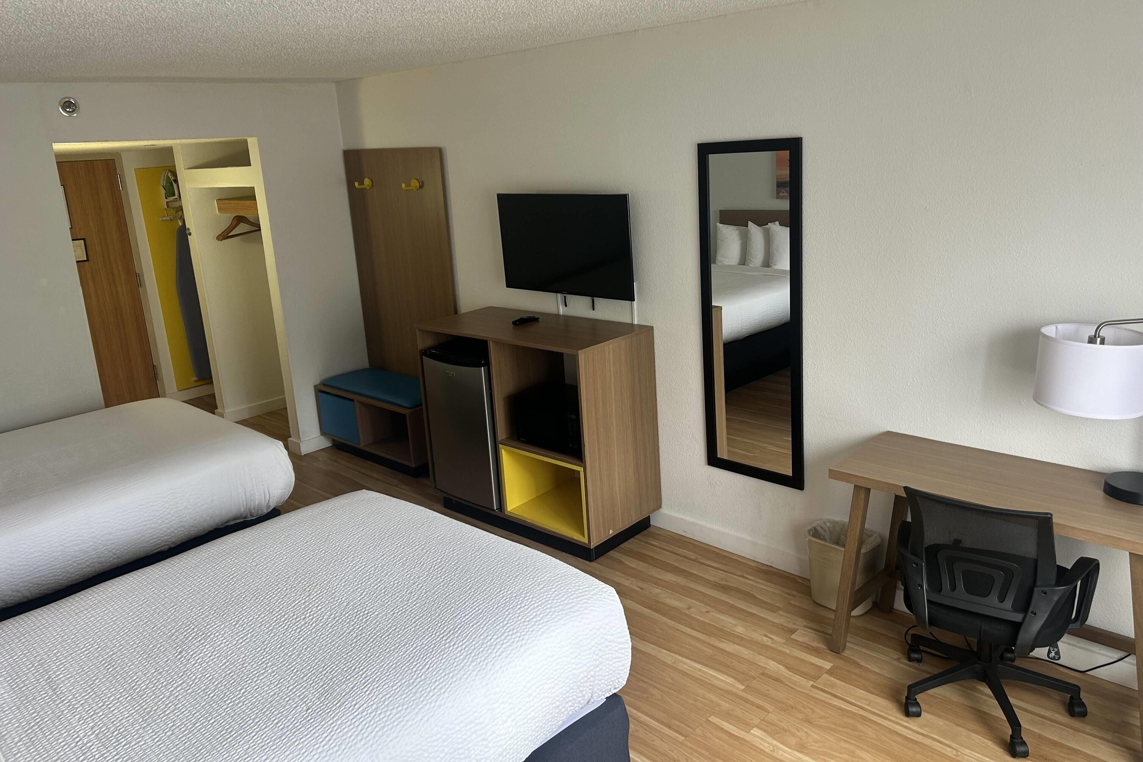 A hotel room with a bed, a desk, a chair, a TV, a mirror, and a wardrobe.