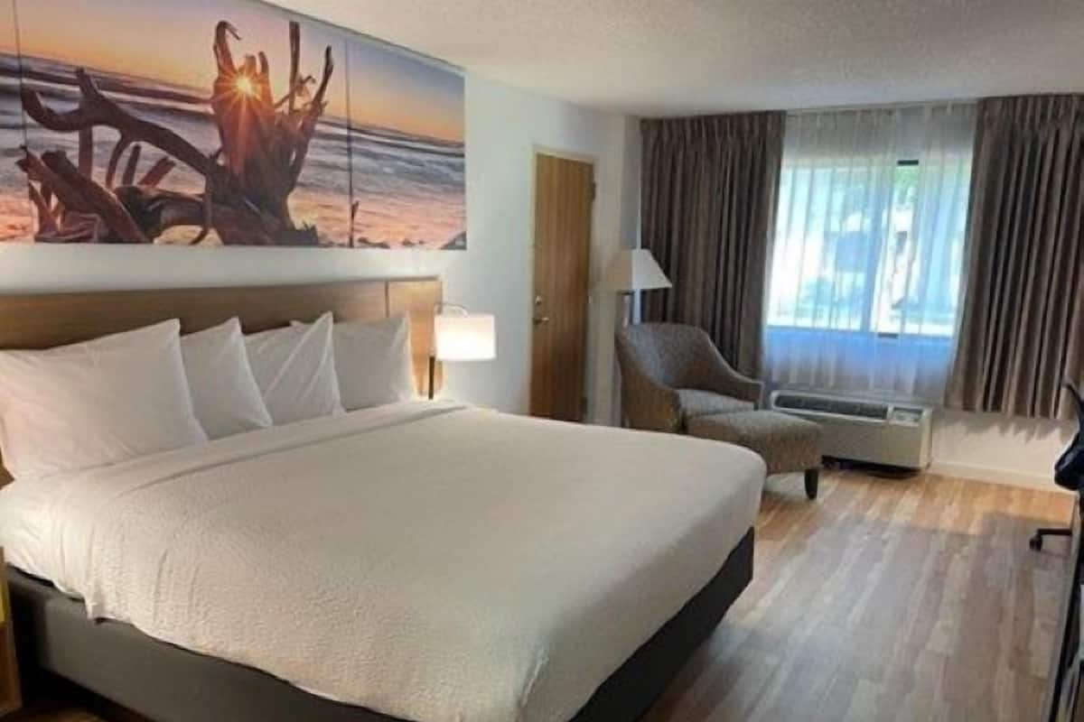 A hotel room with a large bed, a chair, a desk, and a painting on the wall.