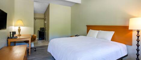 A hotel room with a bed, desk, chair, and a small kitchenette.