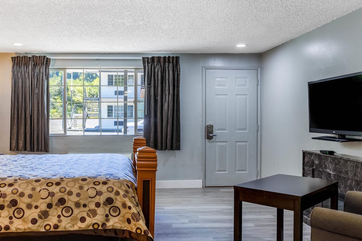 A hotel room with a bed, a TV, a desk, and a window with curtains.