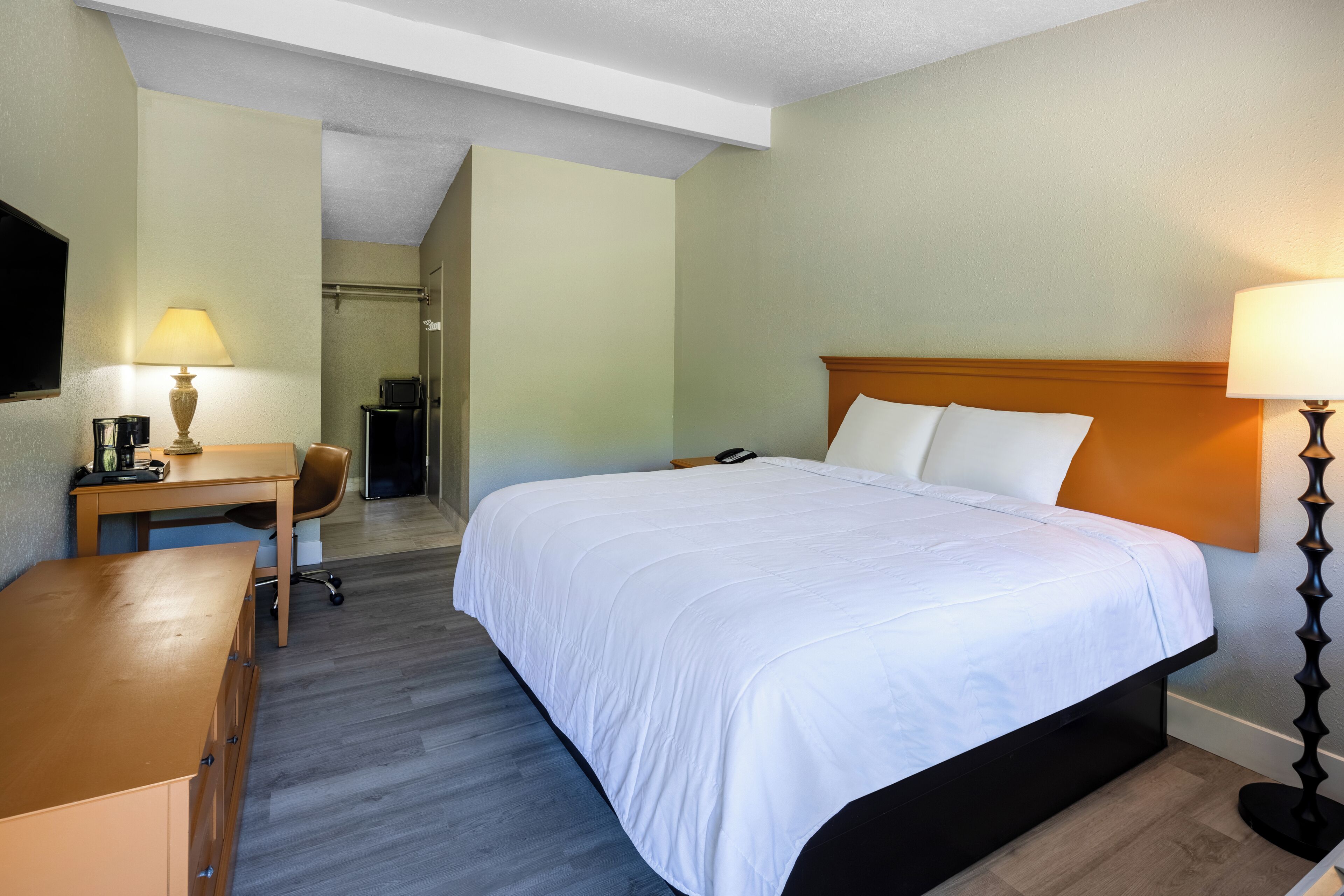 A hotel room with a bed, desk, chair, and a television on the wall.