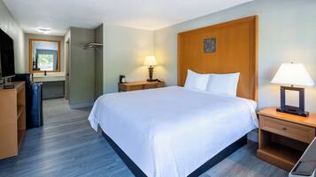 Quarto de hotel com uma cama grande, mesas de cabeceira, escrivaninha, cadeira, espelho e televisão.