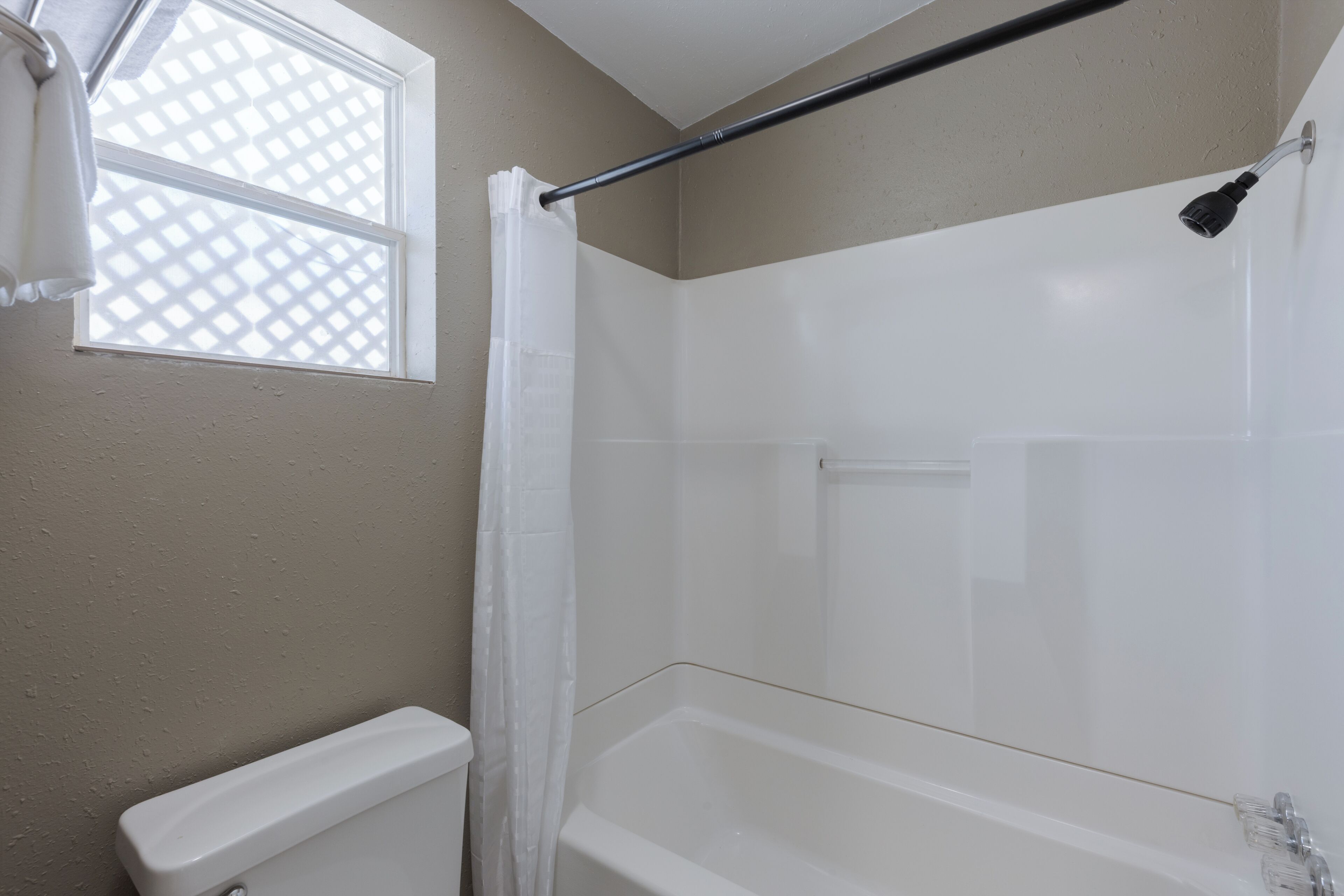 A bathroom with a shower, a toilet, and a window with a lattice design.