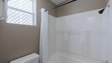A bathroom with a shower, a toilet, and a window with a lattice design.