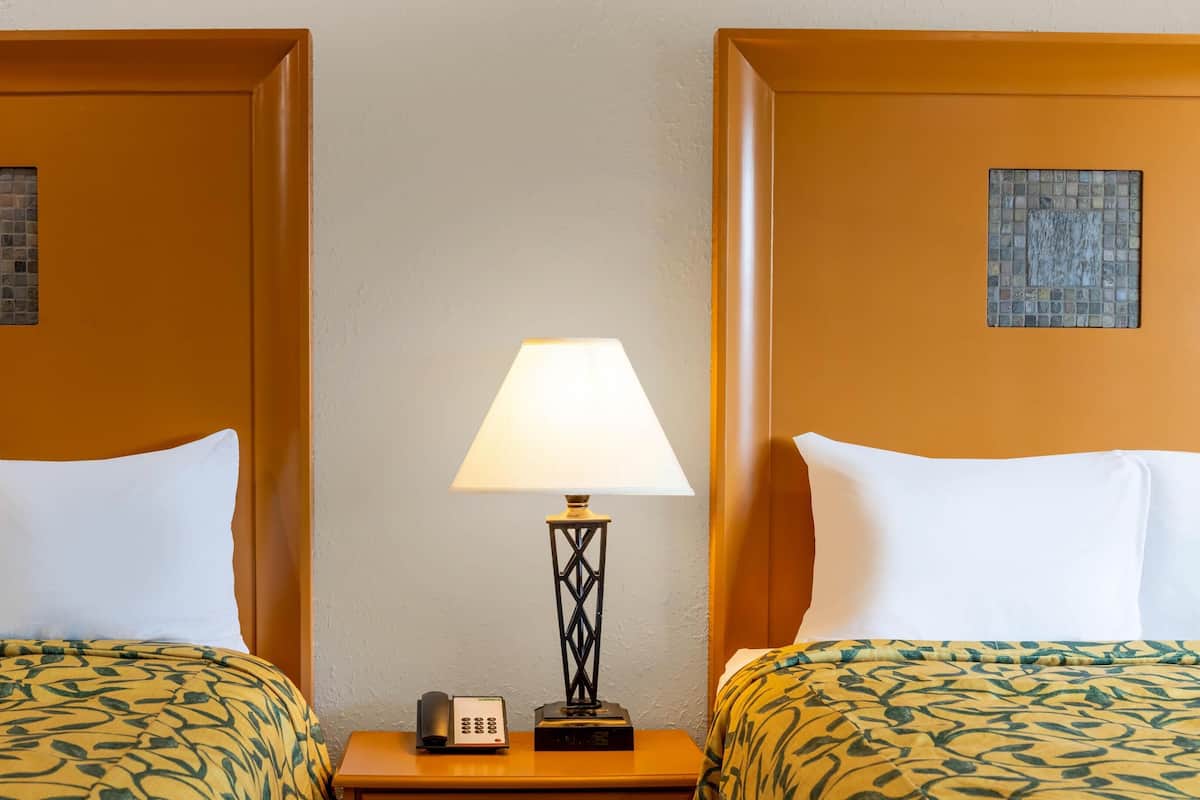 A hotel room with two beds, a nightstand with a lamp, and a telephone.