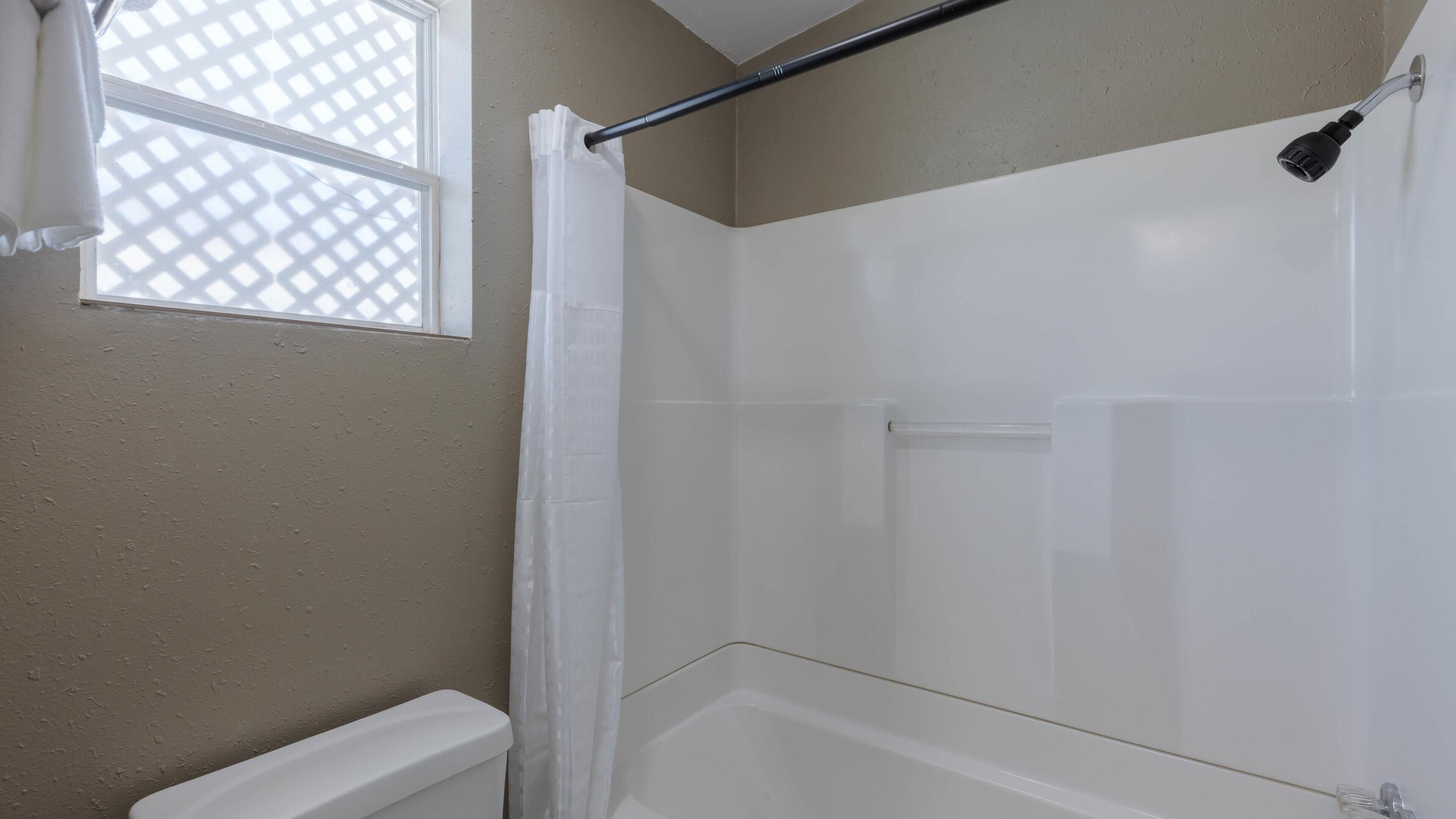 A bathroom with a bathtub, a shower, and a window with a lattice design.