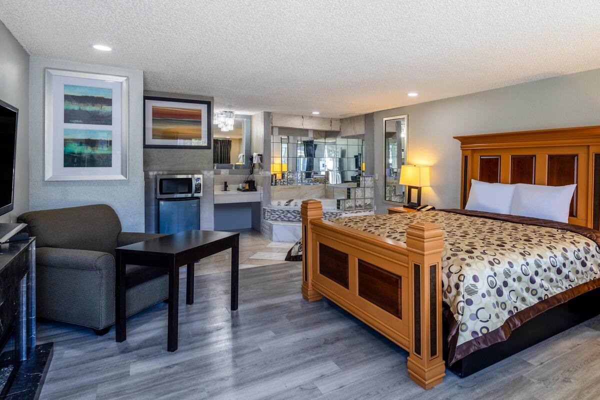 A hotel room with a large bed, a desk, a chair, a microwave, a sink, and a mirror.