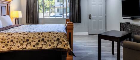 A hotel room with a bed, a TV, a table, and a view of the outside.