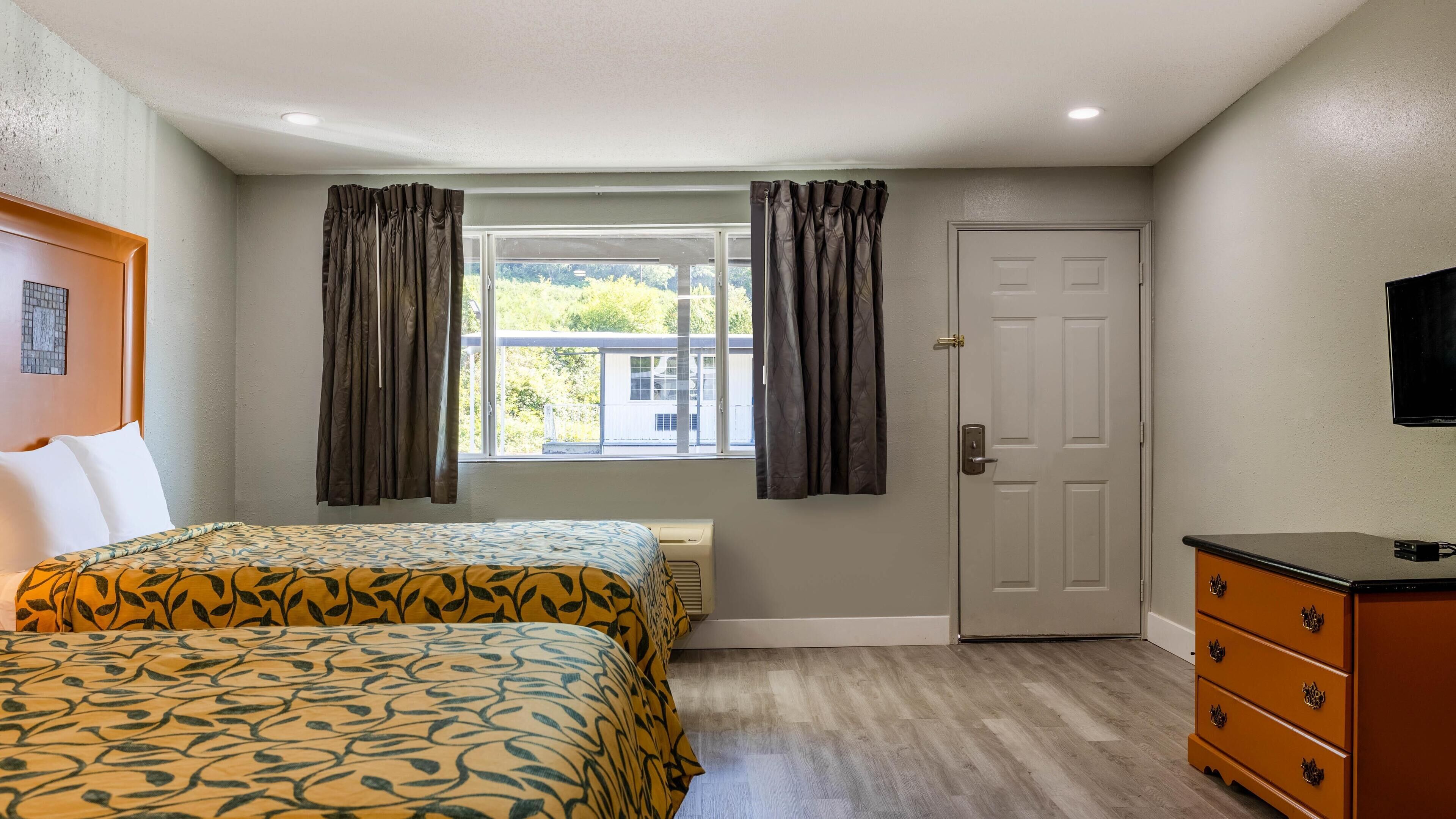 Habitación de hotel con dos camas, una ventana con cortinas, una puerta, un aparador y un televisor en la pared.