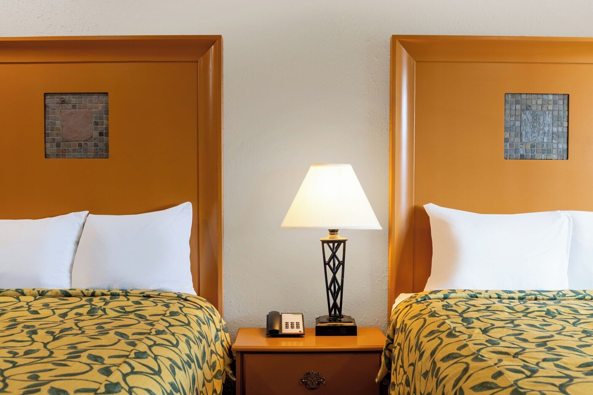 Ein Hotelzimmer mit zwei Betten, einem Nachttisch mit Lampe, einem Telefon und einem kleinen Tisch mit einer Dekoration.