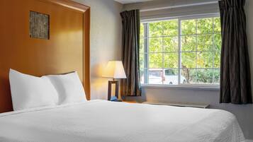 A hotel room with a large bed, a nightstand with a lamp, and a window with curtains.