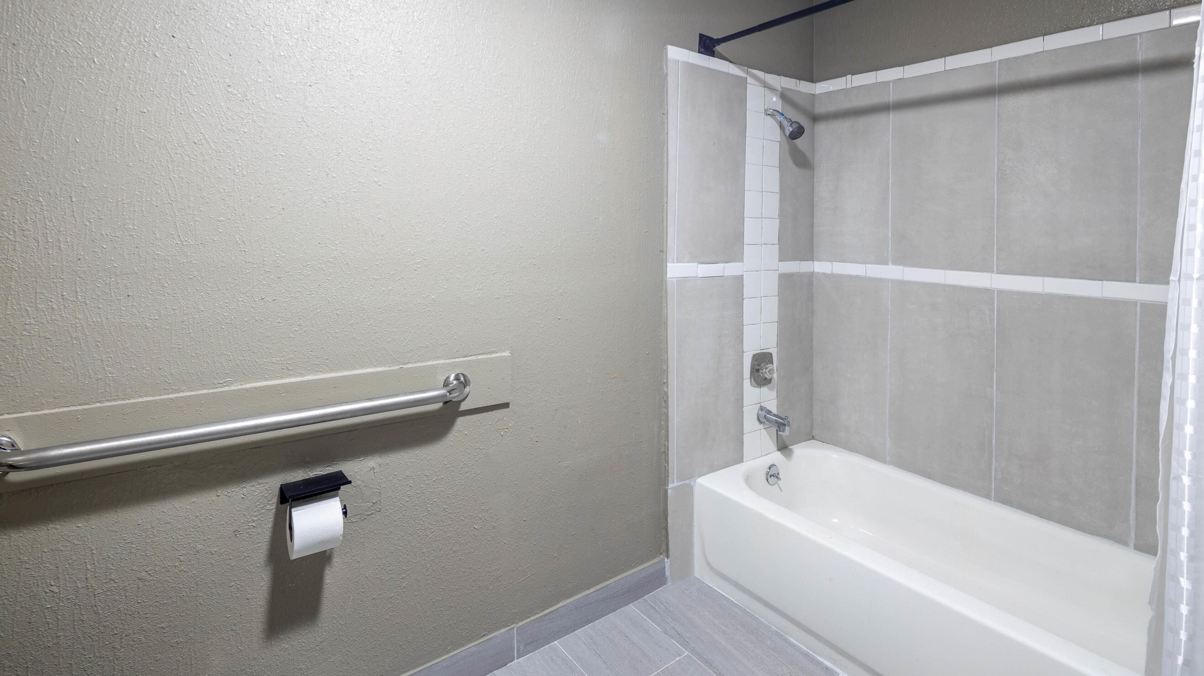A bathroom with a bathtub, a handrail, and a toilet paper holder.