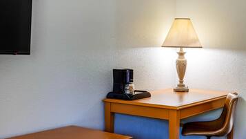 A small wooden table with a coffee maker and a lamp, a chair, and a wall-mounted TV.