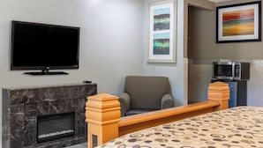 A hotel room with a flat-screen TV, a fireplace, a comfortable chair, a bed with a patterned bedspread, and a microwave.