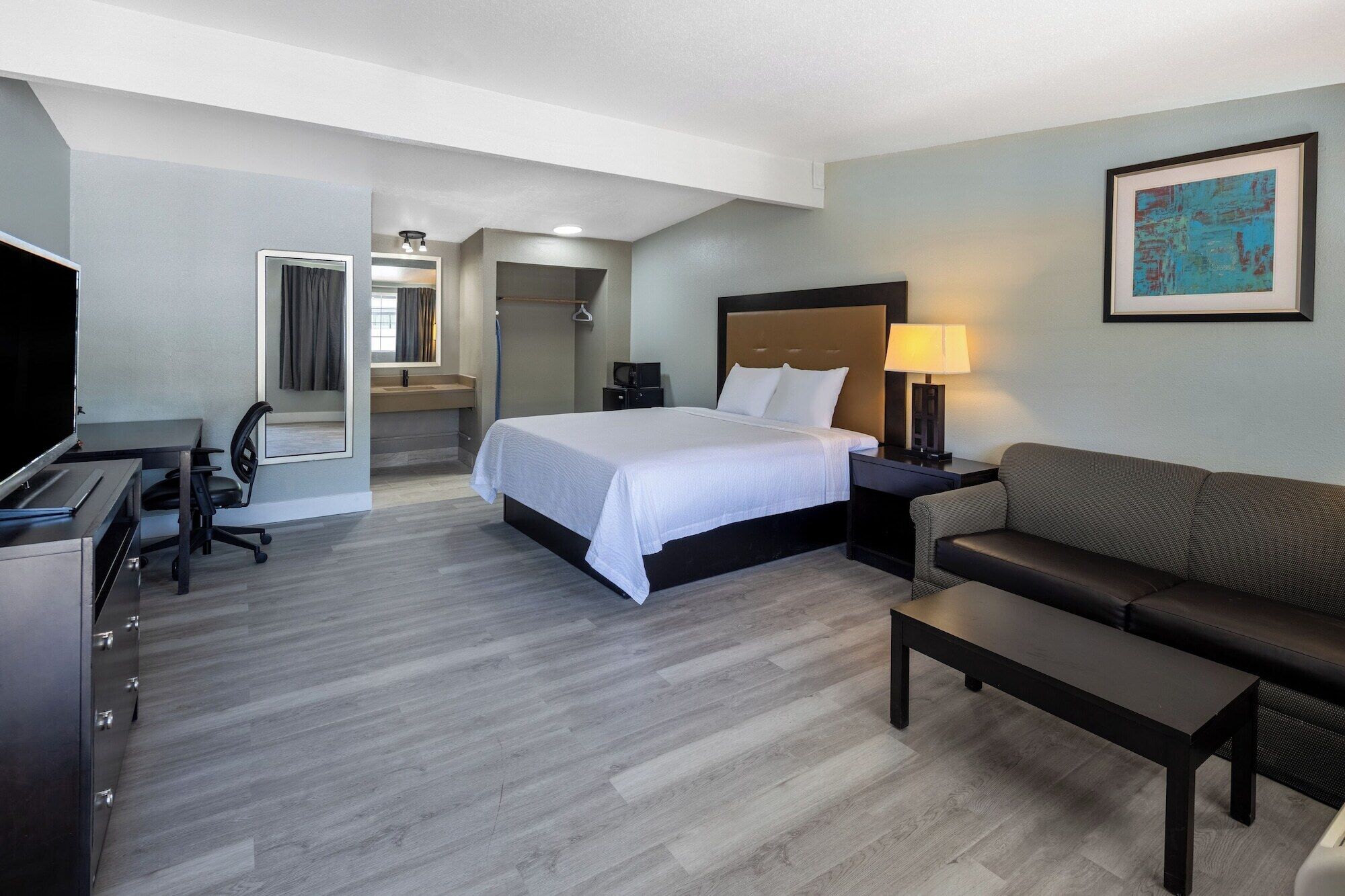 Habitación de hotel con cama, escritorio, silla, sofá, televisor, baño y un cuadro en la pared.