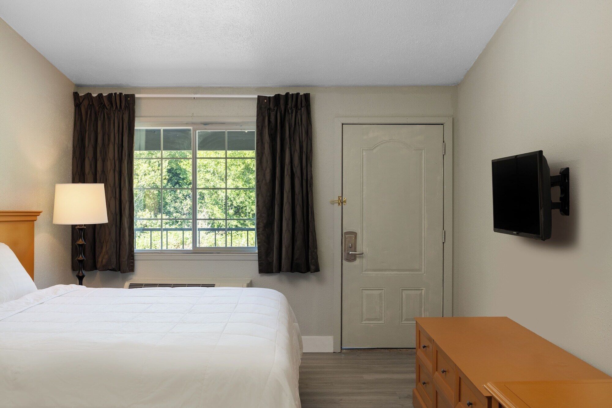 A hotel room with a bed, a desk, a television, and a window with curtains.