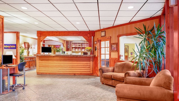 A reception area with a wooden desk, a television, and a reception counter. There are two sofas and a large plant. - Howard Johnson Helena (Helena)