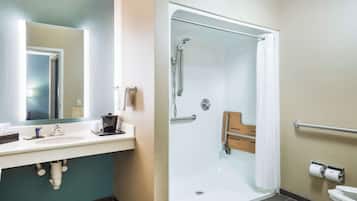 Ein Badezimmer mit Waschbecken, Spiegel, Dusche, Toilette und Haltegriffen.