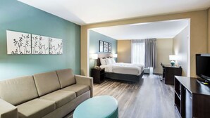 A hotel room with a sofa, a bed, a desk, a TV, and artwork on the wall. - Sleep Inn & Suites Dunmore (Scranton)