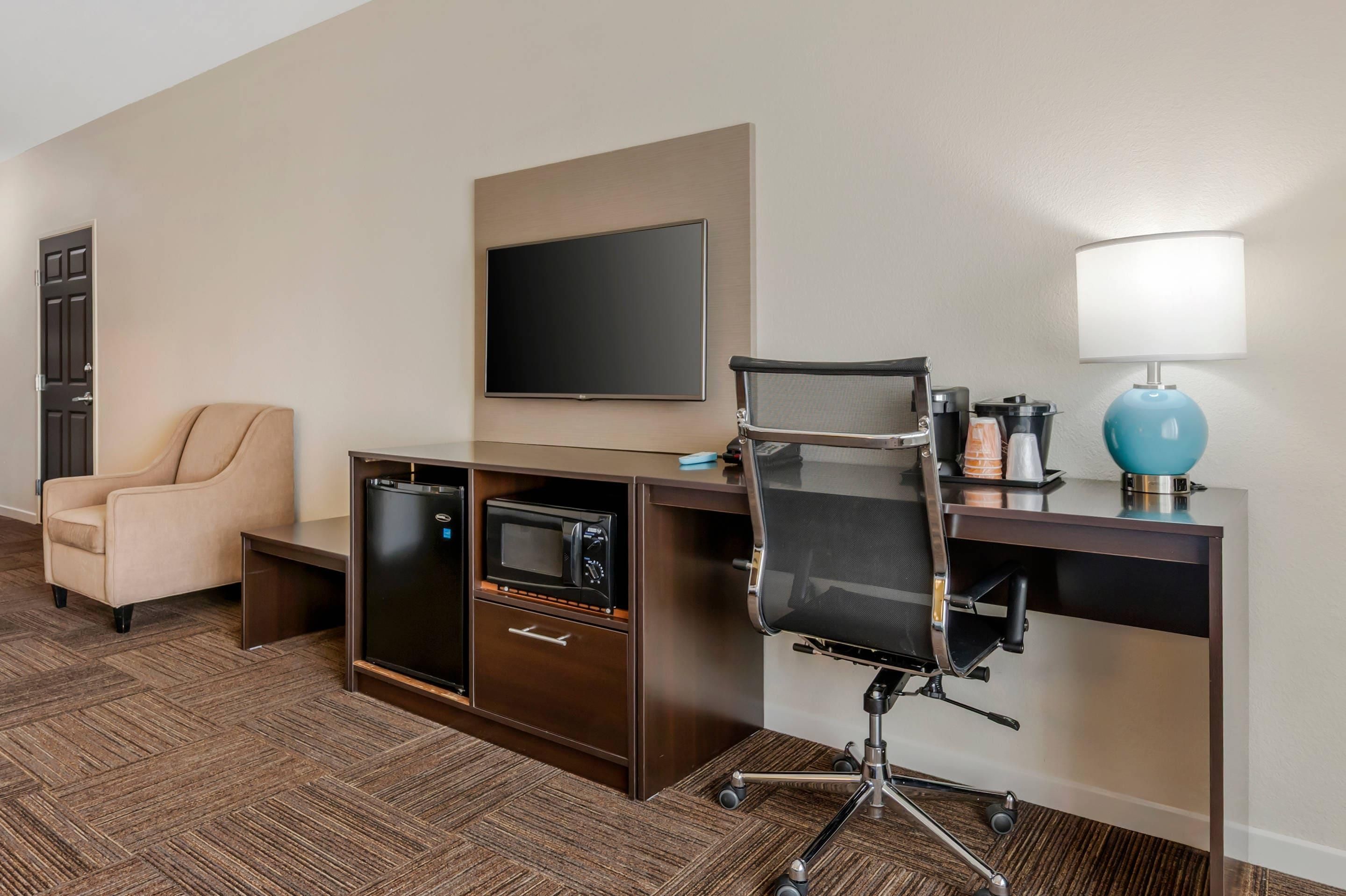 A hotel room with a desk, chair, television, and a coffee machine.